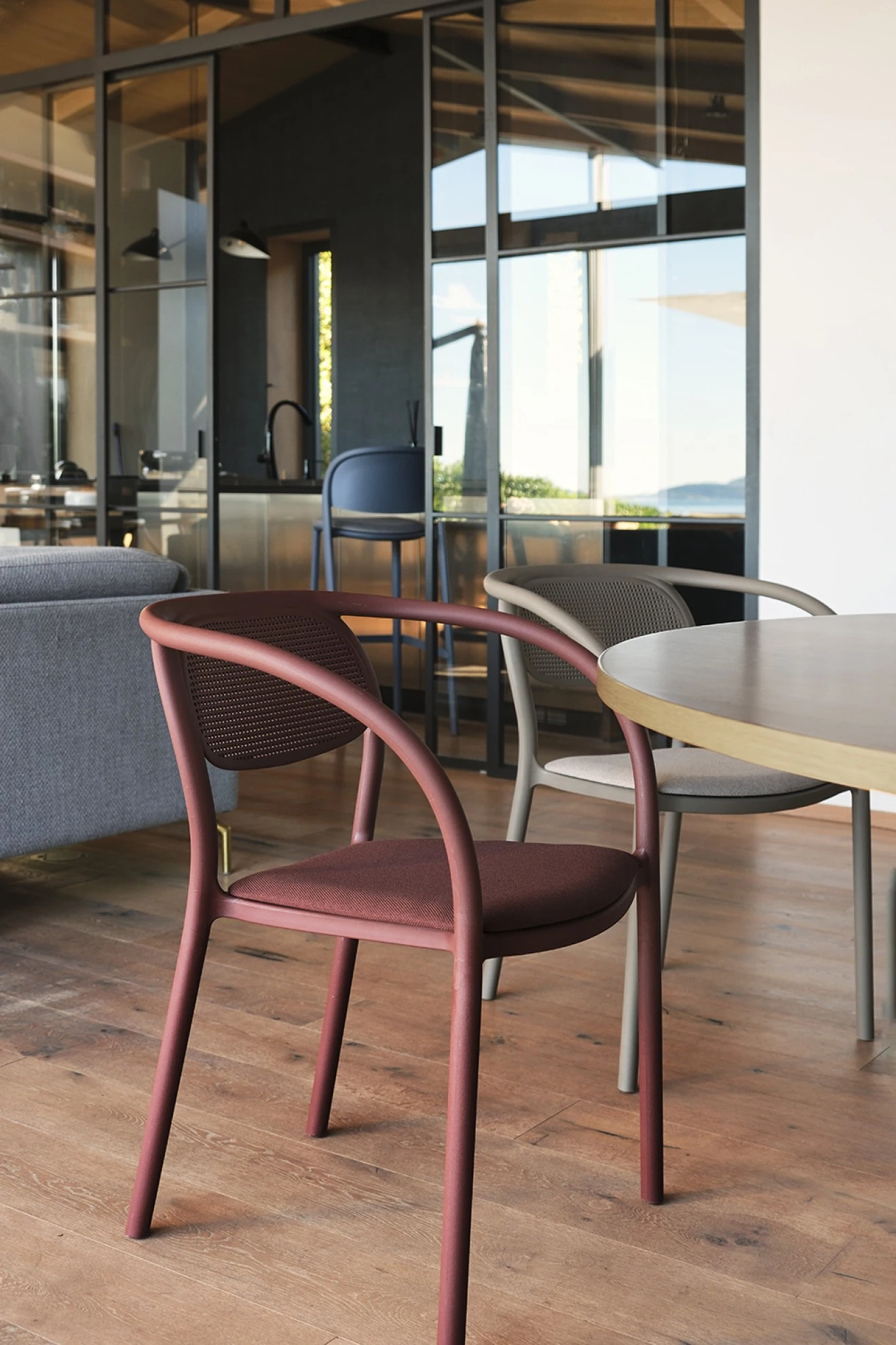 Silla de Ezpeleta en color burdeos junto a una mesa en un interior acristalado.